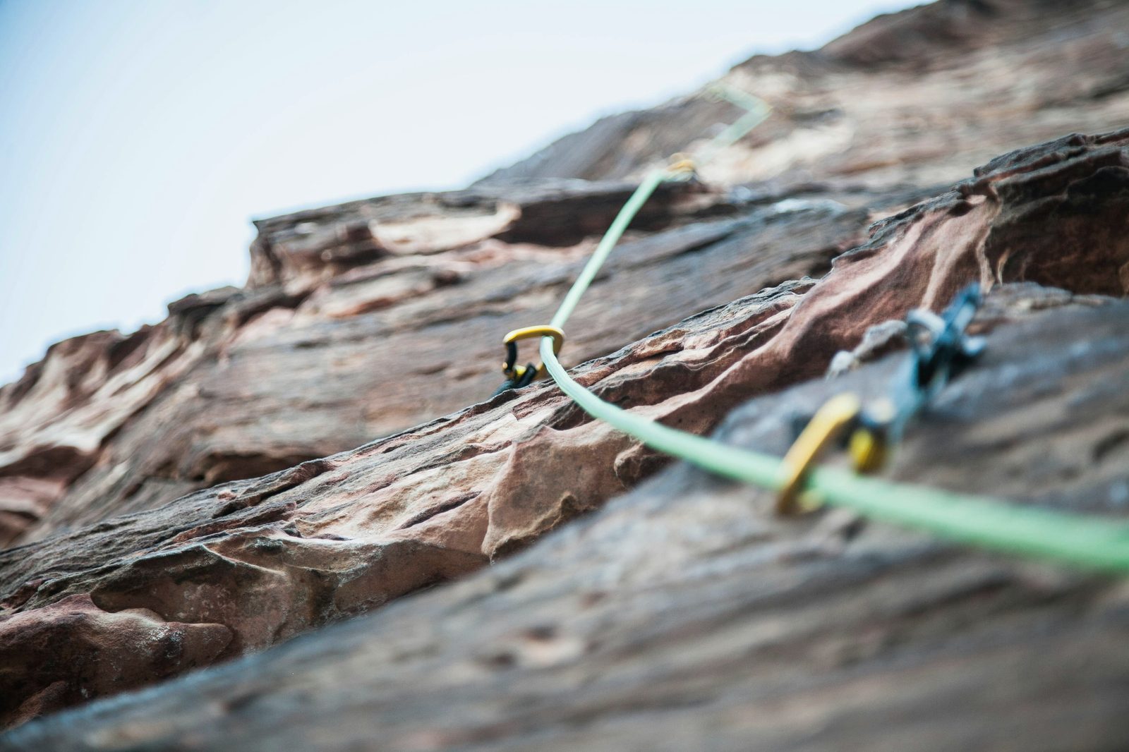 Grünes Kletterseil mit Karabinern an einer Felswand
